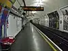 The interior of a building with rounded ceiling and walls, red benches along the left wall, advertisements along the right wall, and a yellow line on the floor