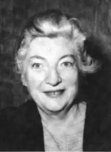 A smiling older white woman with grey/white hair, wearing a dark jacket