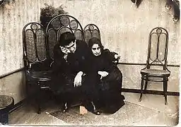 Black and white photo showing a man and a woman, dressed in black, crying, sitting on chairs.