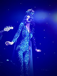 A color photograph of Marina performing live in front of a blue blackdrop.