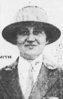 A white woman, smiling, in a brimmed hat, jacket, shirt, necktie