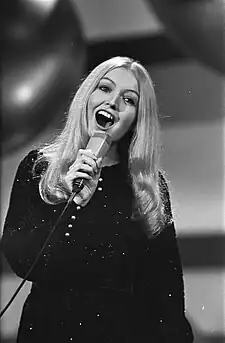 A black and white photo of a young blonde-haired woman holding a microphone and singing