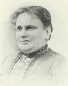 A middle-aged white woman wearing a high-collared dress