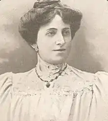 Sepia portrait photo of a woman with dark hair in an up-do, wearing a white high-neck blouse and a necklace.