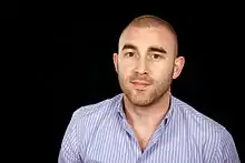 close-up of Matt Mason wearing a light blue and white-striped shirt, smiling at camera