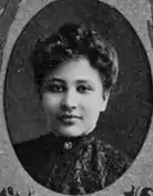 An oval yearbook photograph of a young African-American woman wearing a high-necked ruffled blouse. Her hair is in a bouffant updo.