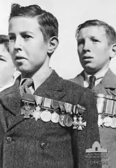 Black and white photograph of three boys. The two boys in the centre and right-hand side of the photo are wearing formal suits with medals pinned on the left-hand side of their chest. Only part of the head of the third boy is visible on the left-hand side of the photo.