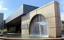 An image of the fountain in front of the main entrance. The design is a circle inside of a square with water falling down from the top of the circle into a pool.