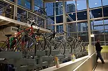 Side view of bikes parked in indoor bike racks, with tall windows beyond the racks