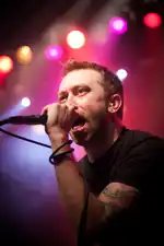 A man holding a mircophone sings in front of a red and blue background.