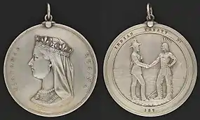 Photograph showing the two sides of a round silver medal, showing the profile of Queen Victoria on one side and the inscription "Victoria Regina", with the other side having a depiction of a man in European garb shaking hands with a man in historical First Nation clothing with the inscription "Indian Treaty 187"