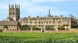 A large building with spires and a tower pictured from a green lawn with a blue sky