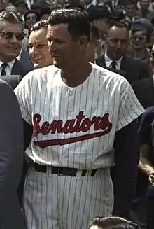 A man in a white baseball uniform with "Senators" on the chest in red