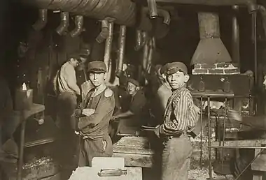 Two adolescent child laborers with dirty faces working in a glass factory at midnight