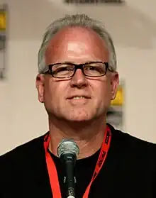 A man with grey hair and glasses sitting in front of a microphone.