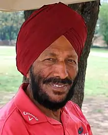 A Sikh man in his late 70s in a red turban and pink T-shirt with beards.