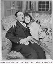 young white man with pencil moustache with young white woman, reclining together on a sofa