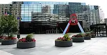 A color photograph of an office building. A pyramid-shaped sculpture stands in front of it.