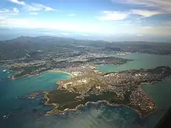 A sprawling city on a peninsula as seen from an aircraft. The landmass is pocketed with many bays and coves.