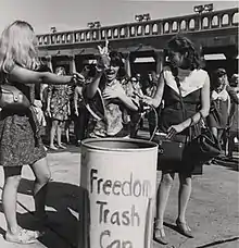 Women toss feminine items in a trash can as a form of protest about female sexualization and oppression