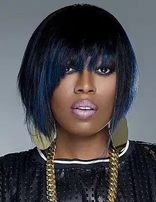 Missy Elliott posing on a grey background wearing a black shirt and gold jewelry.