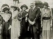 Harding stands beside Marie Curie. Curie has her arm around Harding's. Others stand around them.