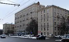 Large gray multi-story building, with trees and cars parked in front