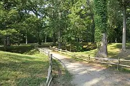 Park with rustic fence, small road, and hills