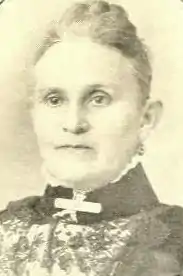 An older white woman wearing a high-collared dress.