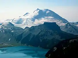 Prominent mountain rising over a smaller steep-sided, flat-topped mountain and a turquoise-coloured alpine lake.