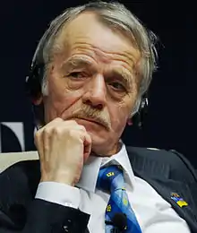 Mustafa Dzhemilev dressed in a dark jacket, white shirt and blue tie, listening to a translation headset.