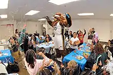 A bear is standing on a chair spraying silly string onto many children and parents watching.