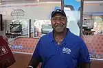 A man, wearing a blue shirt and black cap, is posing for a photo.