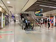 View of the NEL platforms with an escalator going upwards. Two prints are on the opposite sides of the platform, on the pillars in between the platform screen doors.