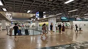 Open concourse with escalators leading downwards to the platforms and Chinese calligraphic writing on the floor.