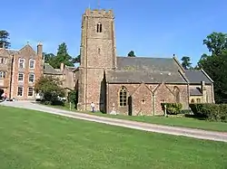 Reddish stone buildings. The church in the foreground has a square tower.