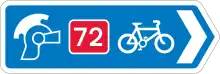 A blue direction sign with a right-pointing arrow. Three symbols (ranged left to right) are; a Roman soldier's helmet, the number 72 written in white on a red background, and a bicycle symbol.