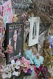 Photographs, flowers, and cards attached to a metal fence.