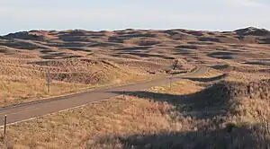 Dune-like hills covered with brown grass; highway running through foreground