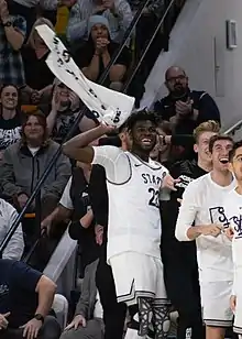 Queta waving a towel and smiling on the sideline