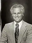 Black-and-white photo of a man with a wide smile and short curly hair wearing a light-colored suit