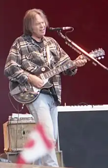 Neil Young performing onstage playing and singing into a microphone