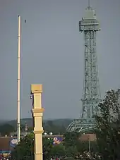 A barely visible figure stands on a tightrope connected by a large pole and a replica of the Eiffel Tower