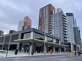 A low grey building with a projecting canopy stands in front of tall residential buildings