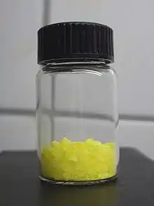 Watch glass on a black surface with a small portion of yellow crystals