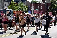 Protesters march down the middle of a street, carrying pink signs reading "No Justice No Pride"