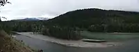 A small sand beach on the edge of a small river, with trees lining the river outside the beach