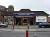 A brown-bricked building with a rectangular, dark blue sign reading "NORTHWOOD HILLS STATION" in white letters all under a blue sky with white clouds