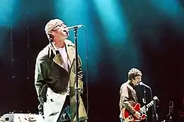 A color photograph of Noel and Liam Gallagher of the band Oasis on stage