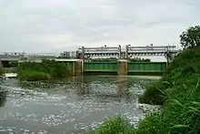 Metal gates surmounted by a gantry across the river. To the left is a weir.